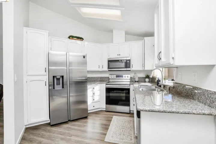 Contemporary kitchen featuring white cabinetry, stainless steel appliances, speckled stone countertops, wood-finish flooring, and a skylight