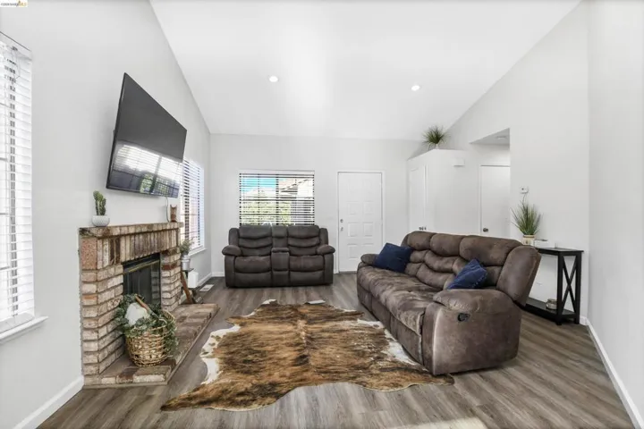 Living area featuring a brick-surround fireplace, wood-finish flooring, vaulted ceilings, and recessed lighting