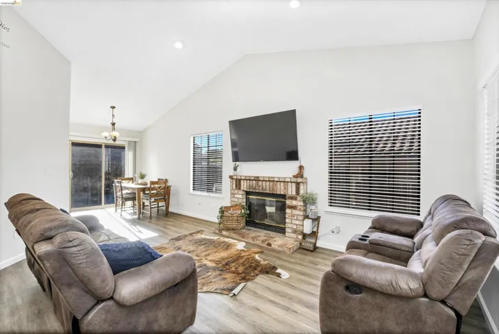 Spacious living area featuring vaulted ceilings, wood-finish flooring, and a brick fireplace