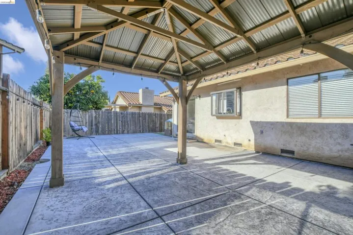 Covered patio with stamped concrete flooring, wood pergola structure, corrugated metal roof, and string lighting