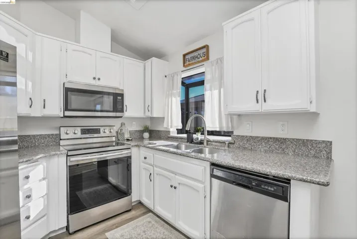 Kitchen featuring white cabinetry, granite countertops, stainless steel appliances, wood-finish flooring, and a double basin sink with a high-arc faucet