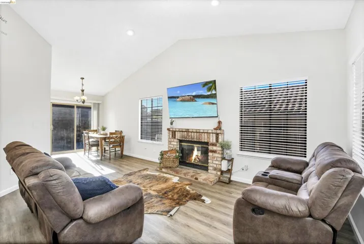 Living area featuring a brick fireplace, vaulted ceiling, and wood-finish flooring