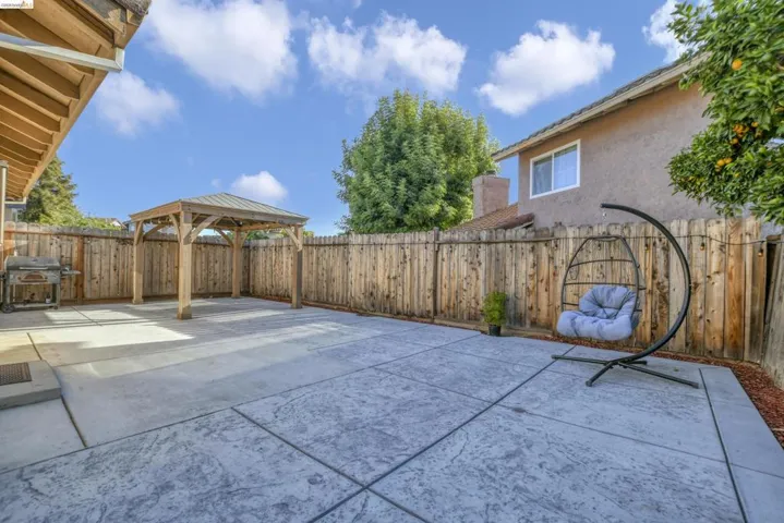 Spacious backyard featuring an expansive stamped concrete patio, a wooden gazebo with a metal roof, and a perimeter wood fence
