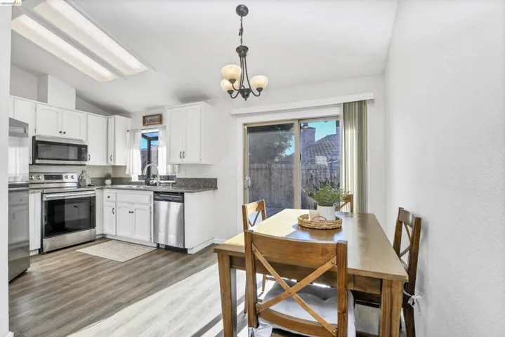 Kitchen dining area featuring wood-finish flooring, white cabinetry, stainless steel appliances, and a sliding glass door