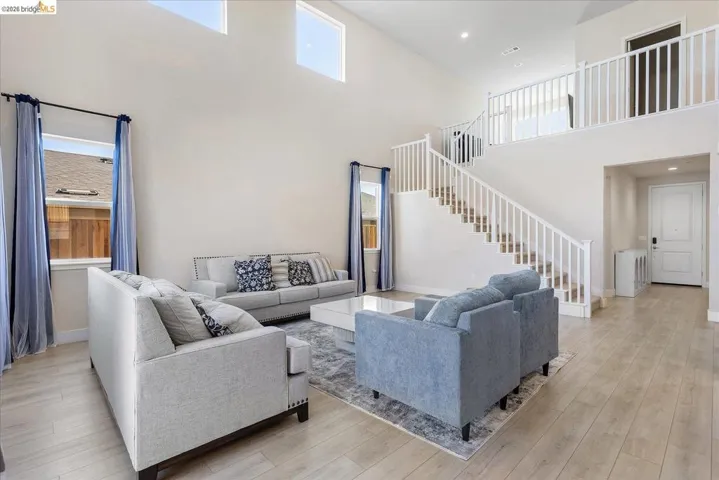 Two-story living area with high ceilings, light wood-finish flooring, and a prominent staircase with white railings