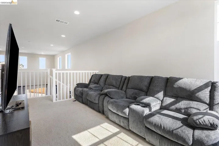 Carpeted loft area featuring recessed lighting, bright white walls, and multiple windows