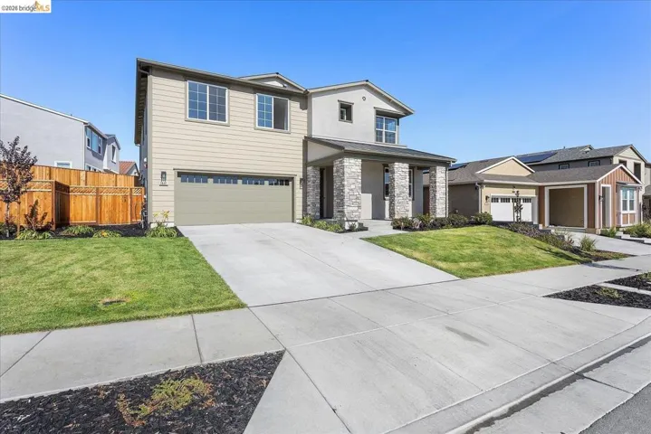Two-story residence featuring a neutral-toned siding exterior, stone facade accents, an attached garage, and a concrete driveway