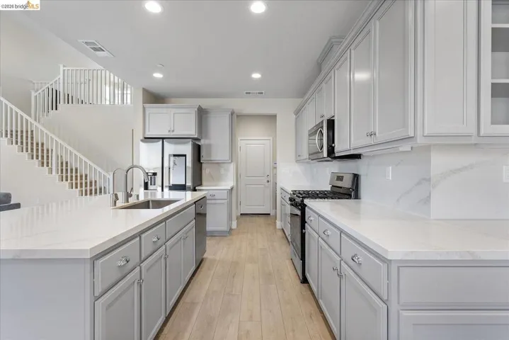 Modern kitchen featuring light wood-finish flooring, white countertops, gray cabinetry, stainless steel appliances, and recessed lighting