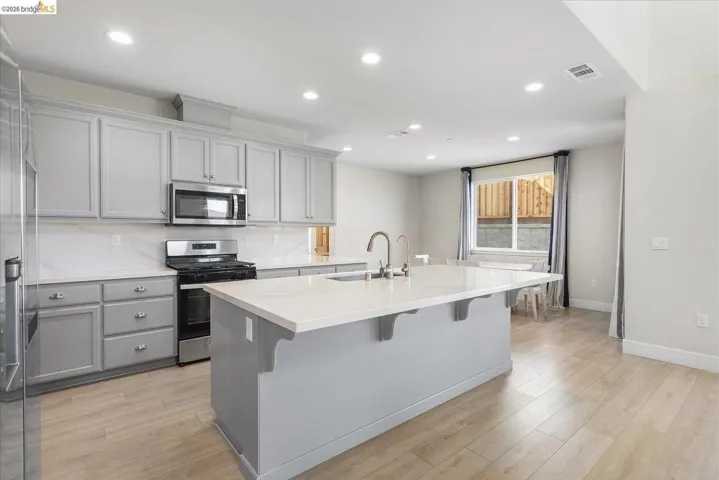 Modern kitchen featuring an expansive center island with an integrated sink, light-toned cabinetry, stainless steel appliances, recessed lighting, and wood-finish flooring