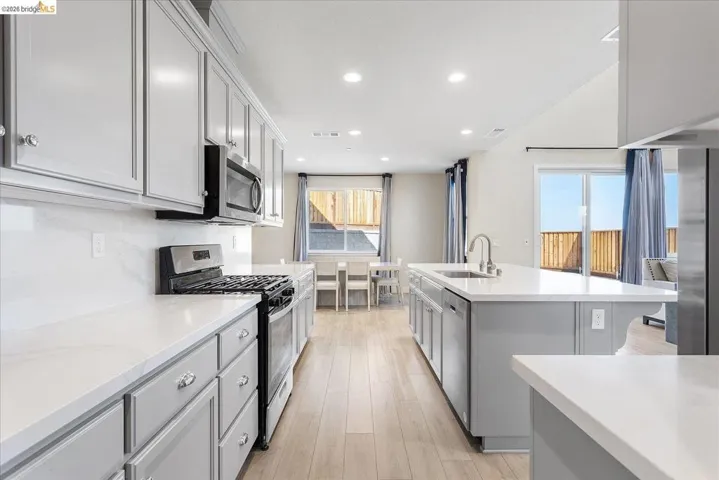 Contemporary kitchen featuring light wood-finish flooring, light grey cabinetry with polished hardware, white countertops, and stainless steel appliances