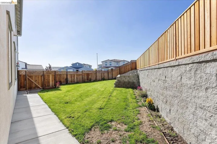 Expansive backyard featuring a concrete retaining wall, wood fencing, and a manicured lawn