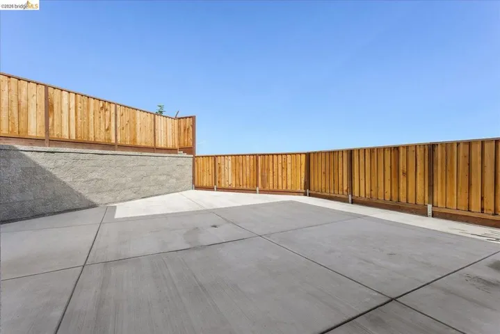 Expansive concrete patio area featuring a retaining wall and wood privacy fencing