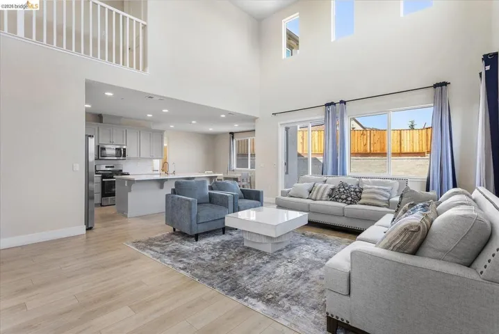 Open-concept living space featuring high ceilings, wood-finish flooring, a contemporary kitchen with stainless steel appliances, and a sliding glass door to the exterior