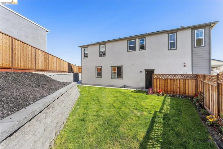 Rear exterior of the property featuring a manicured lawn, block retaining wall, and wood fencing