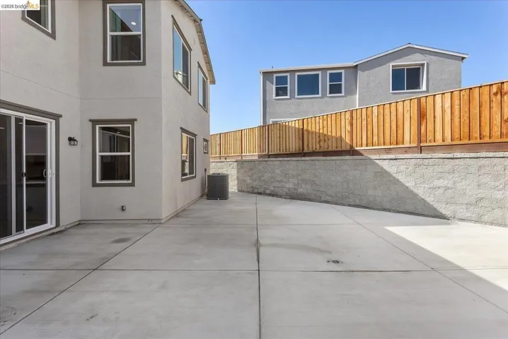 Expansive concrete patio with sliding glass doors, contemporary exterior lighting, and a retaining wall featuring a new privacy fence