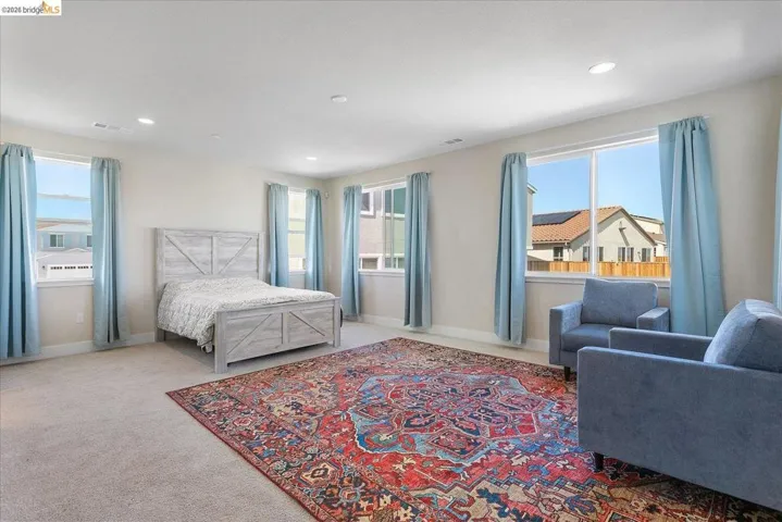 Spacious room featuring neutral carpeting, multiple windows with light blue drapery, and recessed lighting