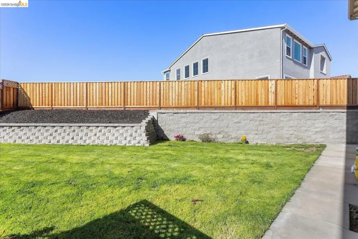 Expansive lawn area featuring a concrete pathway and a substantial retaining wall