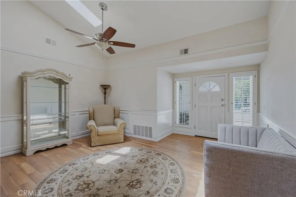 Entry to home living room including vaulted ceiling, skylights, plank tile floors and ceiling fan with light.