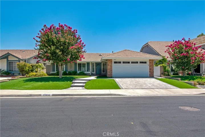 Straight on view of home including, artificial grass, crape myrtle tree in bloom, interlocking concrete paver driveway and walkway and primary entrance to home.