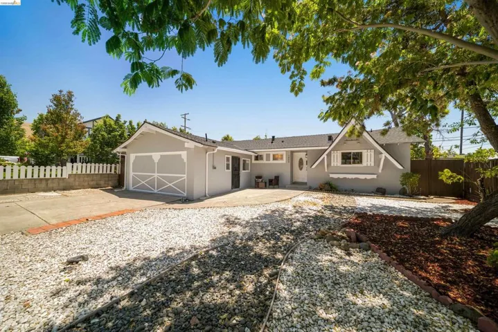 Ranch-style exterior featuring a light gray facade with white trim, a single-car garage with decorative cross-bracing, a prominent front gable with shutters, a white picket fence, and a gravel driveway