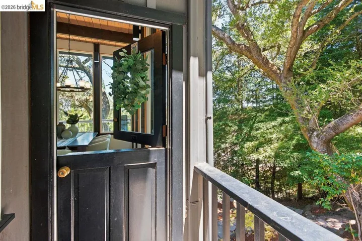 Black Dutch door entrance with brass hardware, opening to an interior space featuring a multi-light chandelier and abundant natural light