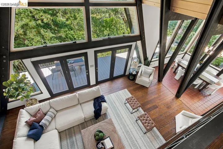 Vaulted ceilings with exposed beams, wood-finish flooring, floor-to-ceiling windows, and French doors opening to an outdoor deck