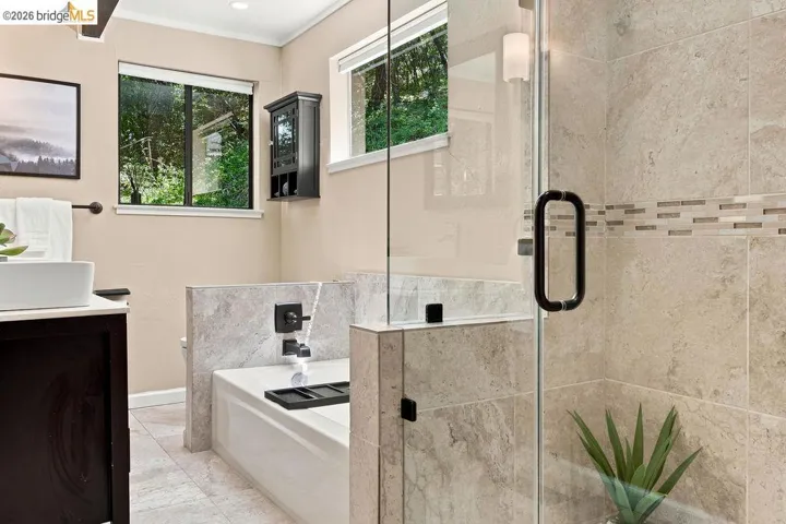 Bathroom featuring a glass-enclosed shower with tile surround, built-in bathtub with tiled deck, a rectangular vessel sink set on a dark wood-finish vanity, and light-toned wall paint