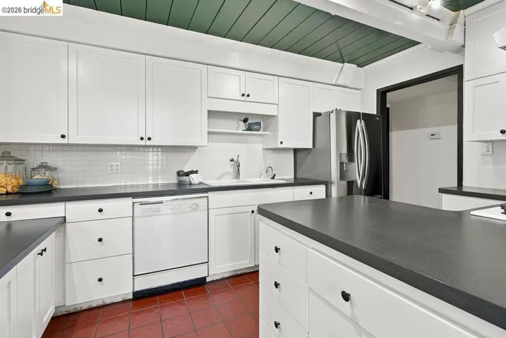 Kitchen featuring white cabinetry, dark countertops, white subway tile backsplash, stainless steel refrigerator, and red tile flooring