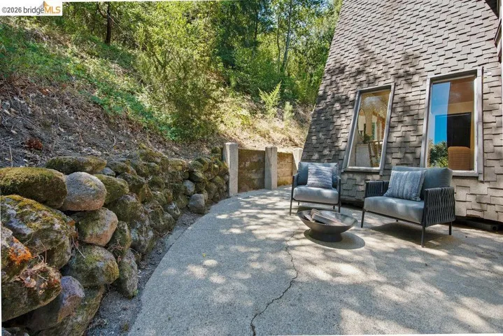 Concrete patio featuring a stone retaining wall and a wood-shingle exterior with two tall, rectangular windows
