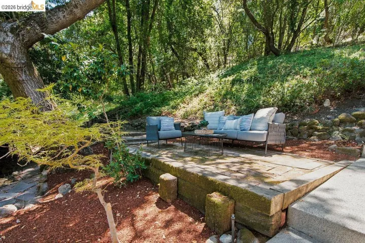 Outdoor entertaining space featuring a tiered wood and stone patio, mature trees, and natural landscaping