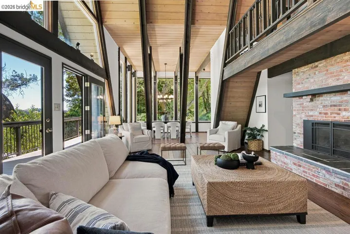 Vaulted ceiling living space featuring exposed wood beams, a brick fireplace with a stone hearth, and extensive window walls