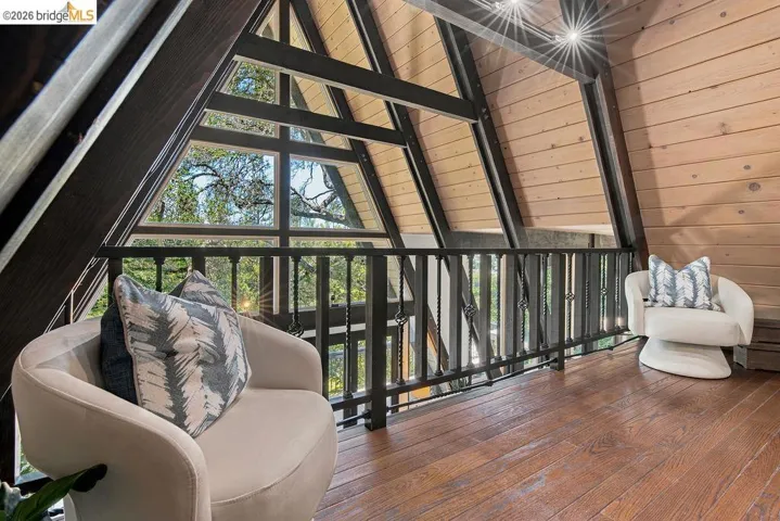 A-frame interior featuring natural wood plank walls, wood-finish flooring, dark exposed beams, and a black wrought iron railing overlooking a multi-pane window