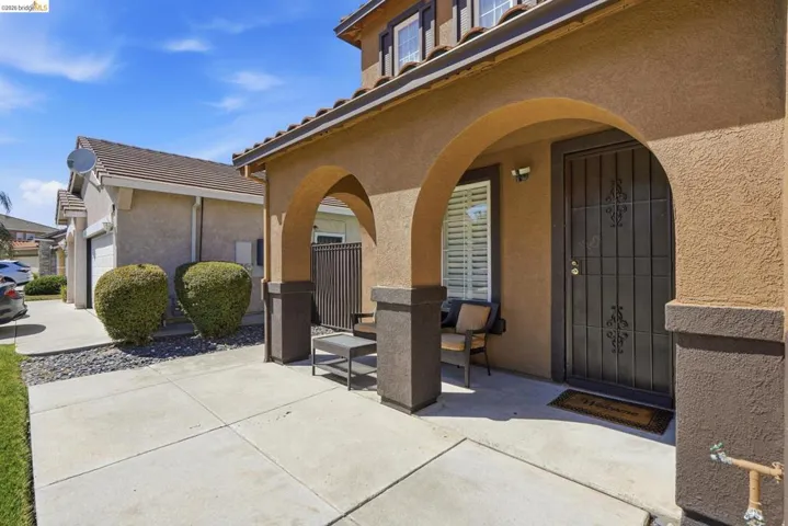Arched entryway featuring a security screen door, stucco exterior, concrete walkway, and a tiled roofline