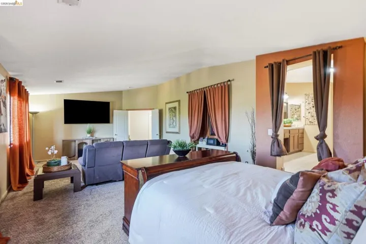 Carpeted room featuring a large wall-mounted screen, a window with drapery, and direct access to a bathroom with a vanity
