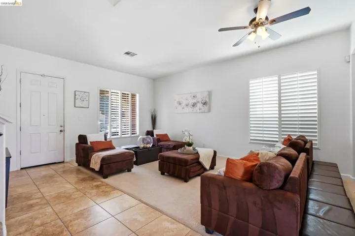 Spacious living area featuring neutral-toned walls, a ceiling fan with integrated lighting, and multiple windows with plantation shutters