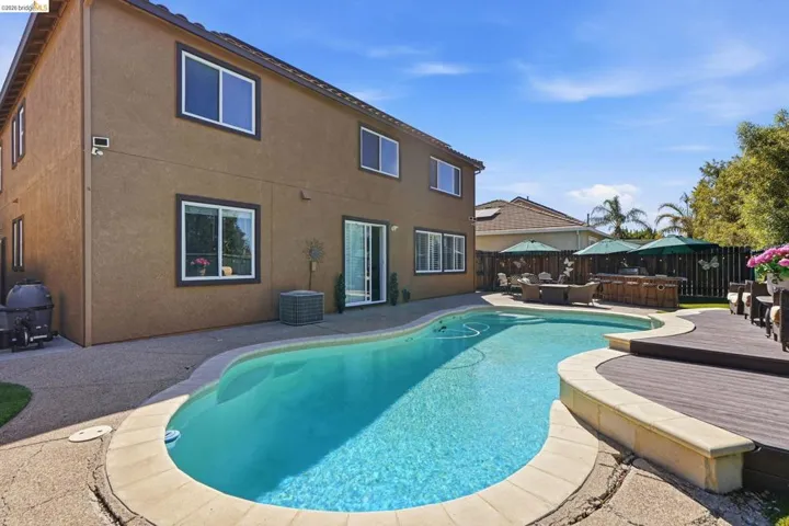 Resort-style backyard featuring a freeform swimming pool, extensive concrete patio, and a separate composite deck area
