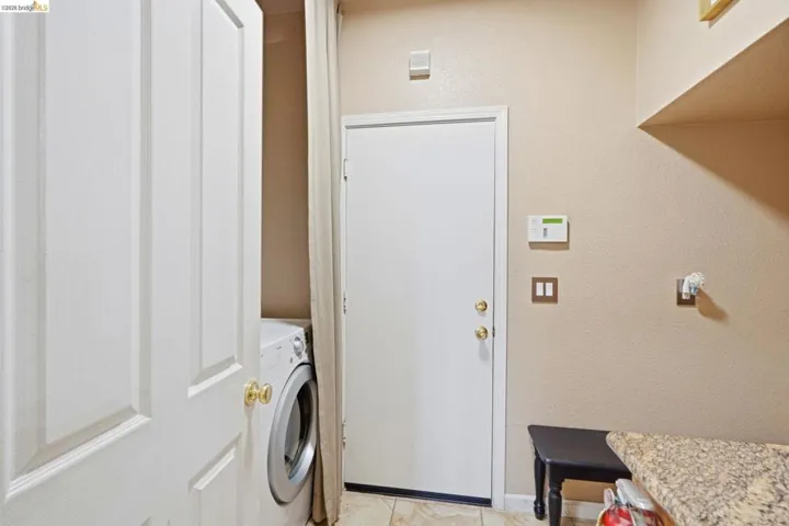 Dedicated laundry area featuring a tile floor, built-in shelving, and a granite-look countertop