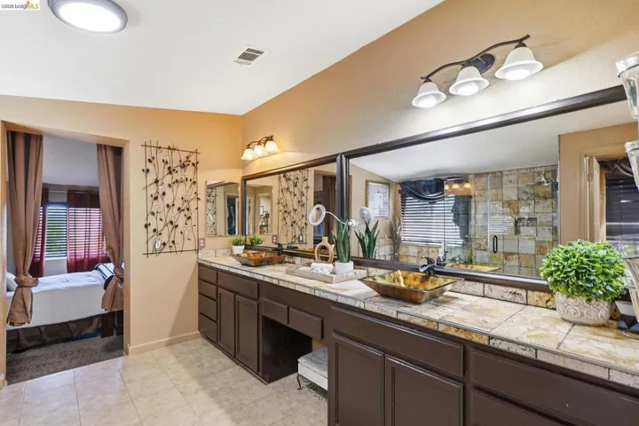 Dual vanity with vessel sinks, tile countertops, dark wood cabinetry, and a full-width mirror