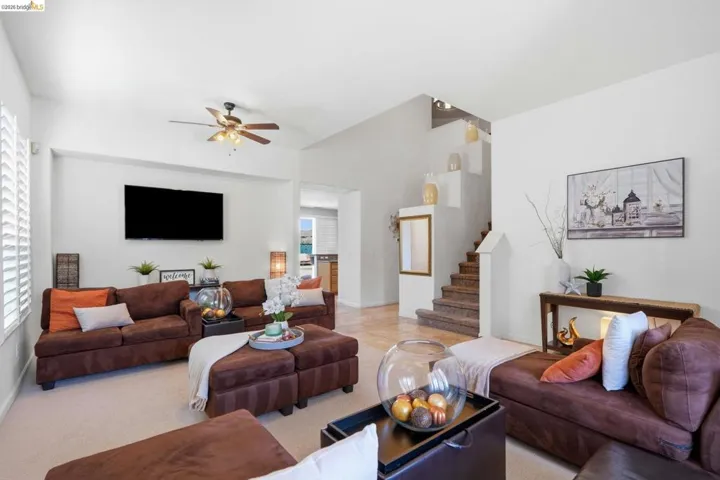 Spacious living area featuring high ceilings, ceiling fan, natural light from a window with plantation shutters, and a staircase with wall niches