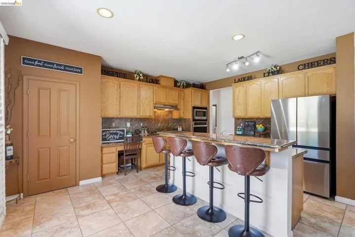Kitchen featuring abundant wood cabinetry, an integrated breakfast bar with seating, stainless steel appliances, a built-in desk area, and tile flooring