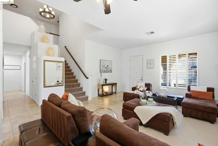 Spacious living area featuring neutral wall tones, plantation shutters, and a chandelier in the stairwell