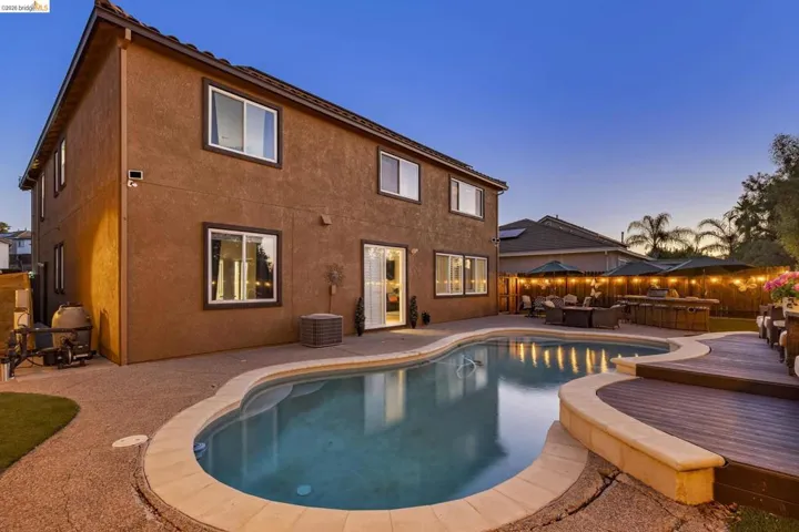 Expansive backyard featuring a custom-shaped swimming pool with concrete decking, a raised wood deck, and a stucco exterior