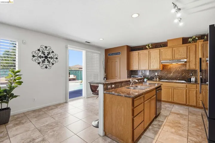 Kitchen featuring a central island with sink, wood cabinetry, stone countertops, and tile flooring