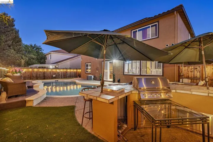 Backyard oasis featuring a built-in outdoor kitchen with a stainless steel grill, a freeform swimming pool with integrated lighting, a composite deck area, and artificial turf