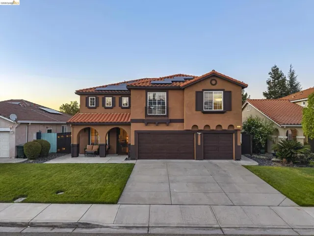 Two-story stucco exterior featuring a tile roof, solar panels, and a three-car garage