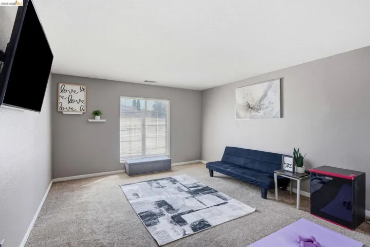 Carpeted interior space featuring light grey walls and a ceiling-mounted television