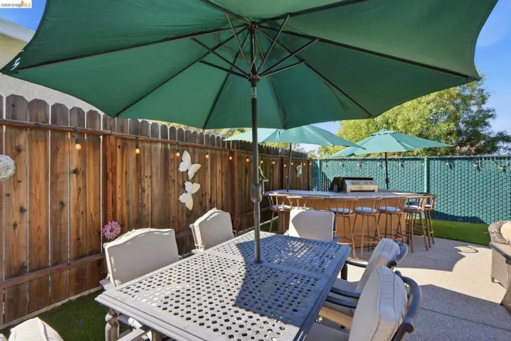 Outdoor patio area featuring a built-in bar with integrated grill, concrete patio, wood privacy fence, and artificial turf