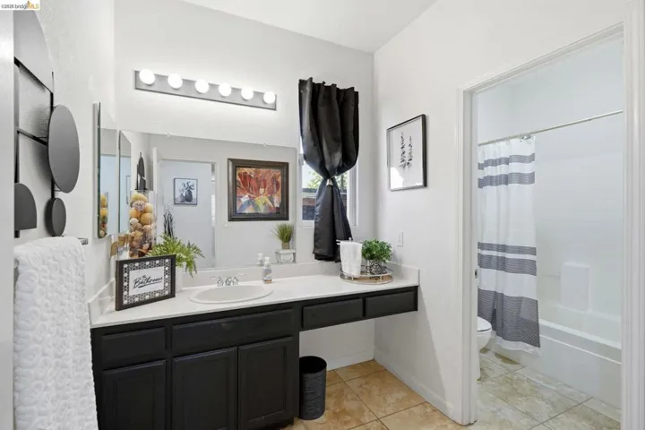 Bathroom featuring a spacious vanity with dark cabinetry, an integrated sink, a large wall mirror, and modern strip lighting