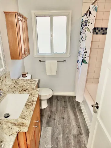 Remodeled bathroom featuring updated vanity and granite countertop, new lighting above the sink, new flooring, cabinet above toilet for added storage and a tiled tub/shower combination.