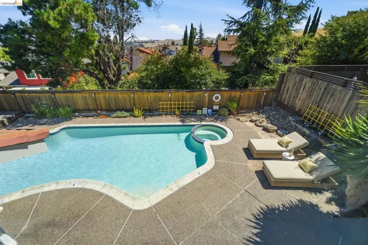 Outdoor pool with integrated spa, bordered by a concrete patio and a wood privacy fence